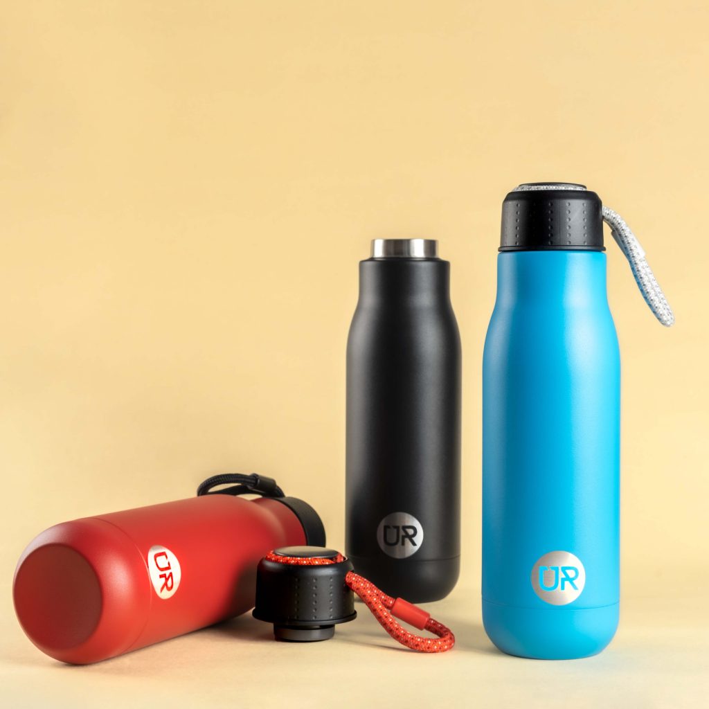 Creative product photography of reusable water bottles. The photo has neutral pastel yellow colour , showing red , blue and black bottles